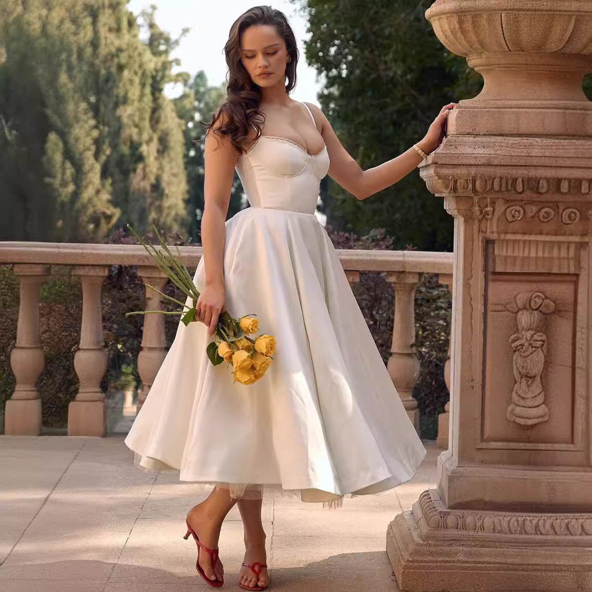 Rochie midi din satin alb cu corset si fusta evazata, purtata pe terasa, accesorizata cu trandafiri galbeni
