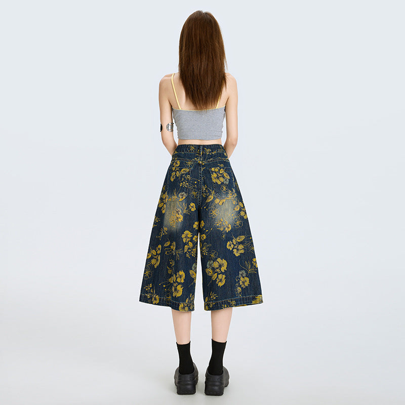 Model vazut din spate purtand Blugi largi cu print floral albastru inchis cu flori galbene, top scurt gri si pantofi negri