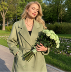 Woman wearing an Adele Double Wool Coat in green, holding a bouquet of roses in a park