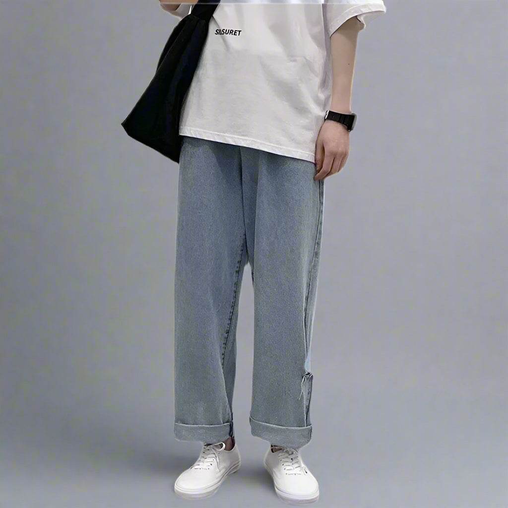 Model purtând blugi largi din denim deschis cu tiv răsucit tricou alb oversize și teniși albi