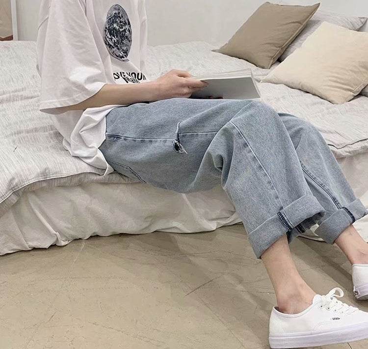 Persoană pe pat purtând blugi largi din denim cu tiv rabatat tricou alb și teniși albi AM Vision RO