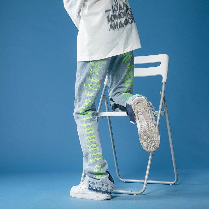 Model purtand Jeans drepți pictați manual bleu cu text verde neon pe picior si adidasi albi fundal albastru