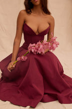 Model purtând o Rochie cu croială maxi și decolteu adânc. bordo fără bretele, corset și orhidee roz.