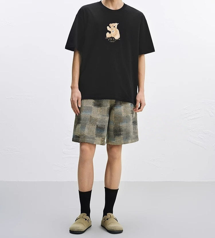 Barbat purtand Tricou cu urs brodat negru oversized asortat cu pantaloni scurti in carouri si sosete negre