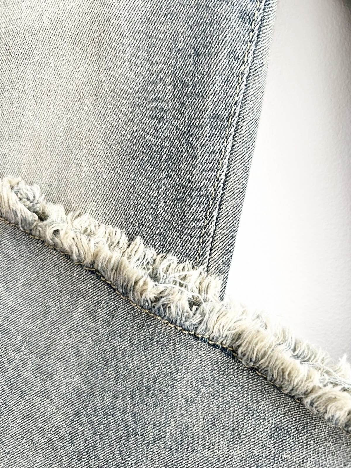 Detaliu cusături și margine franjurată la blugi evazați elastici din denim deschis la culoare