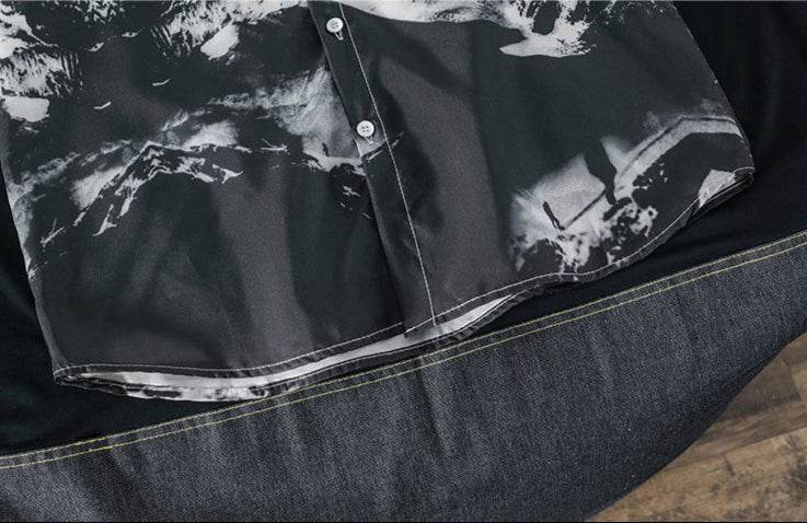 Detaliu cămașă cu imprimeu alb-negru cu nasturi, așezată pe material textil închis la culoare