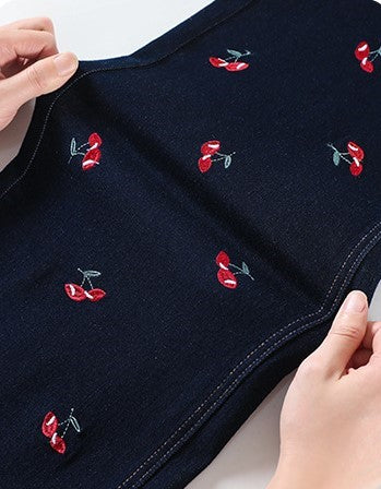 Hands holding Cherry Embroidered Wide Leg Jeans showcasing vibrant cherry embroidery on dark denim