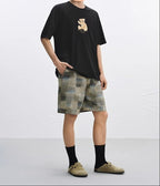 Black AM Vision RO Embroidered Bear T-Shirt paired with patterned shorts for a casual look