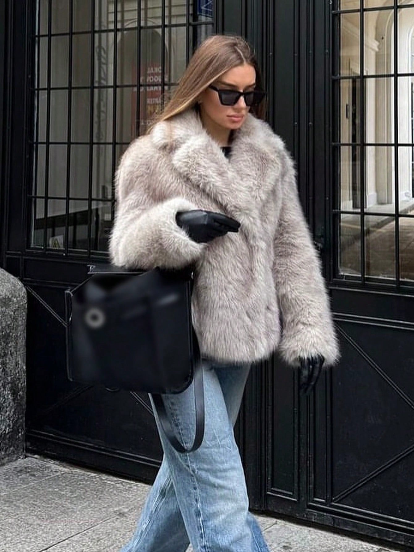 Stylish woman wearing a faux fur effect coat with gloves and sunglasses, walking on the street