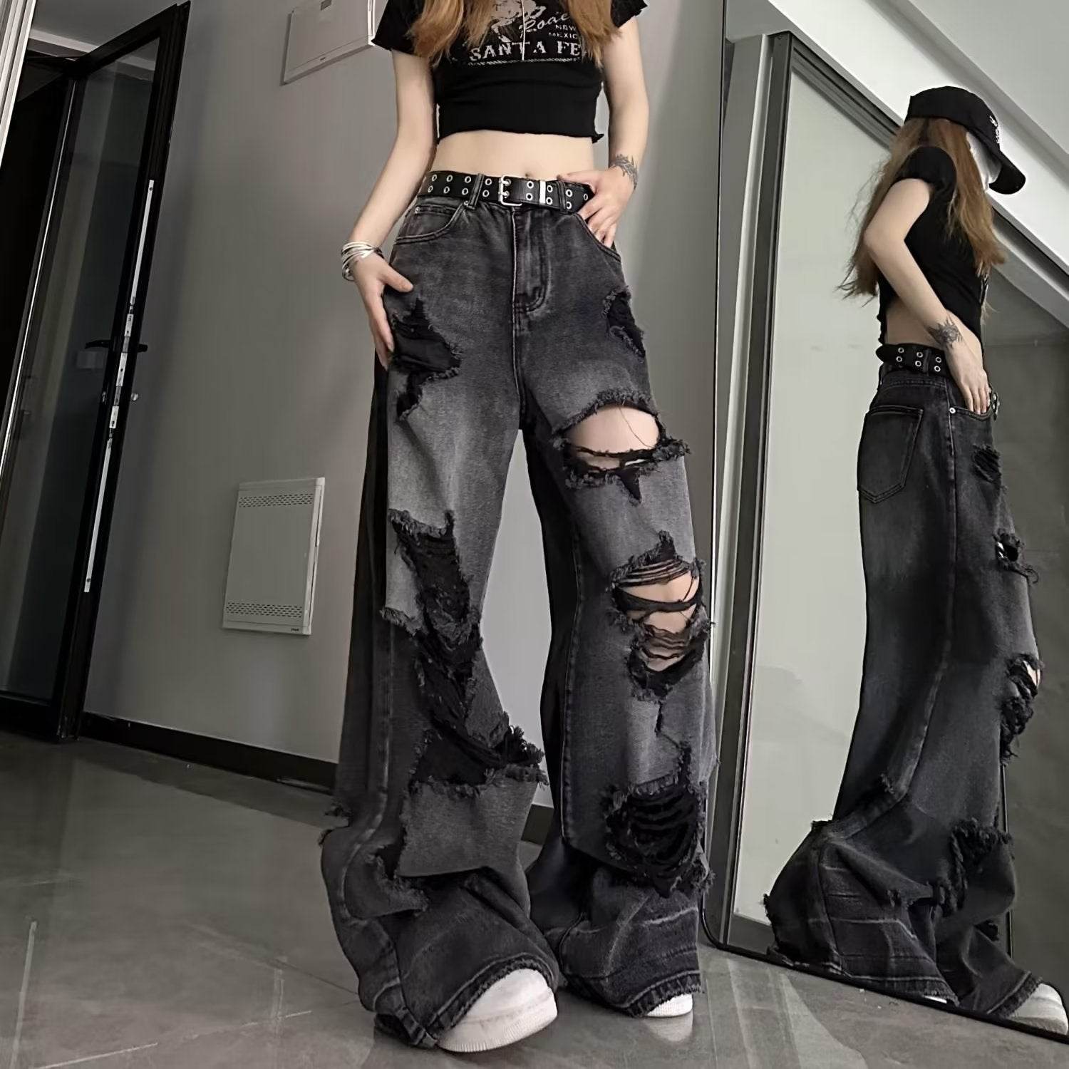 High waisted black ripped baggy jeans with distressed detailing worn by a model in a casual indoor setting
