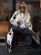 Woman wearing a stylish Long Faux Fur Effect Coat with sunglasses, sipping a drink in a chic setting