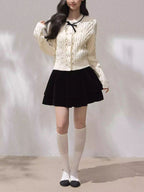 Stylish Moonlight Ribbon Cardigan in cream with a black bow, paired with a black skirt