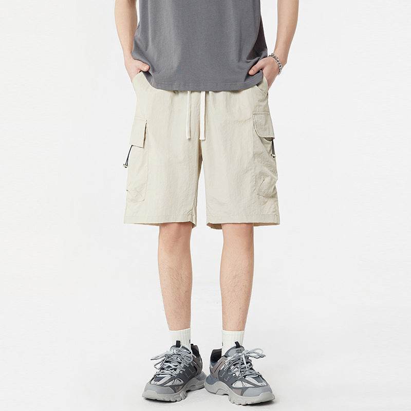 Pantaloni scurți casual cu buzunare multiple de culoare crem purtați de bărbat cu tricou gri și adidași gri