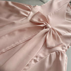 Close-up of the Pink Lotus Bow Princess Dress featuring a large bow detail on satin fabric