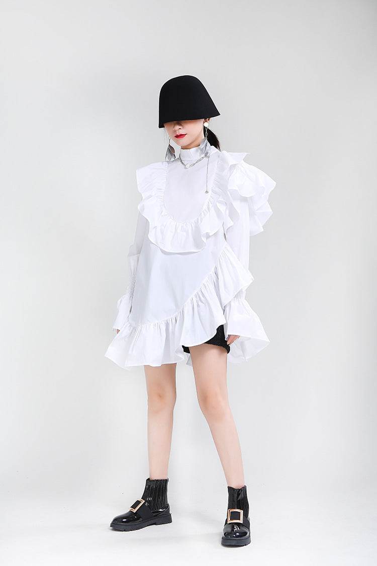 Model purtând o rochie asimetrică cu volane albă, combinată cu cizme negre și pălărie neagră