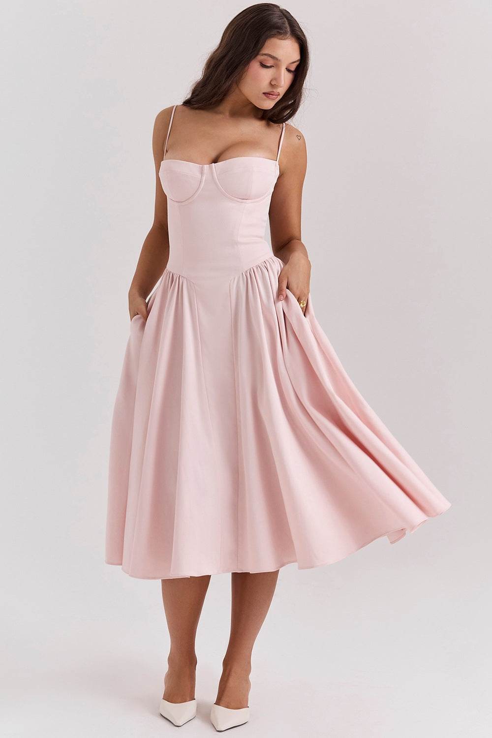 Femeie purtând rochie cu design minimalist roz pal, cu bretele subțiri și fustă evazată pentru ocazii elegante