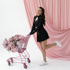 Model wearing the Sculpt Fit Three Piece Set with a pleated skirt and jacket, posing with a pink shopping cart of flowers