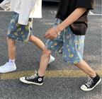 Two people wearing AM Vision RO summer streetwear floral shorts in blue with yellow flowers, styled casually