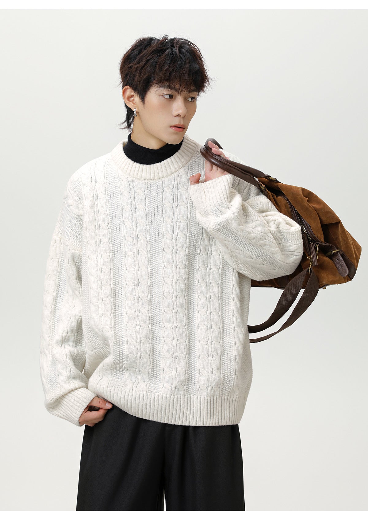 Model wearing a white textured cable knit sweater paired with black pants and a brown shoulder bag