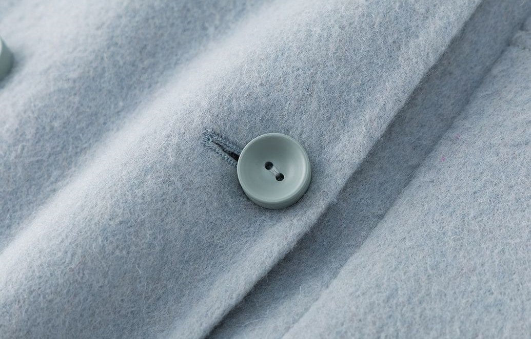 Close-up of a button detail on The Amaya Pastel Coat in soft blue fabric for a stylish look