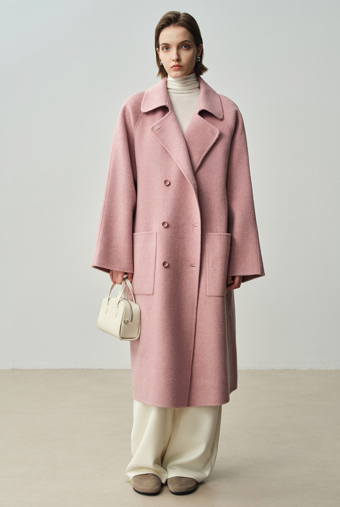 The Amaya Pastel Coat in soft pink, featuring a relaxed fit and large pockets for a stylish look