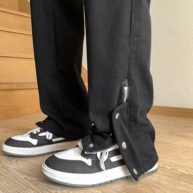 Jeans cu capse la picior negri evazați cu fermoar lateral, purtați peste teniși negri și albi pe podea din lemn